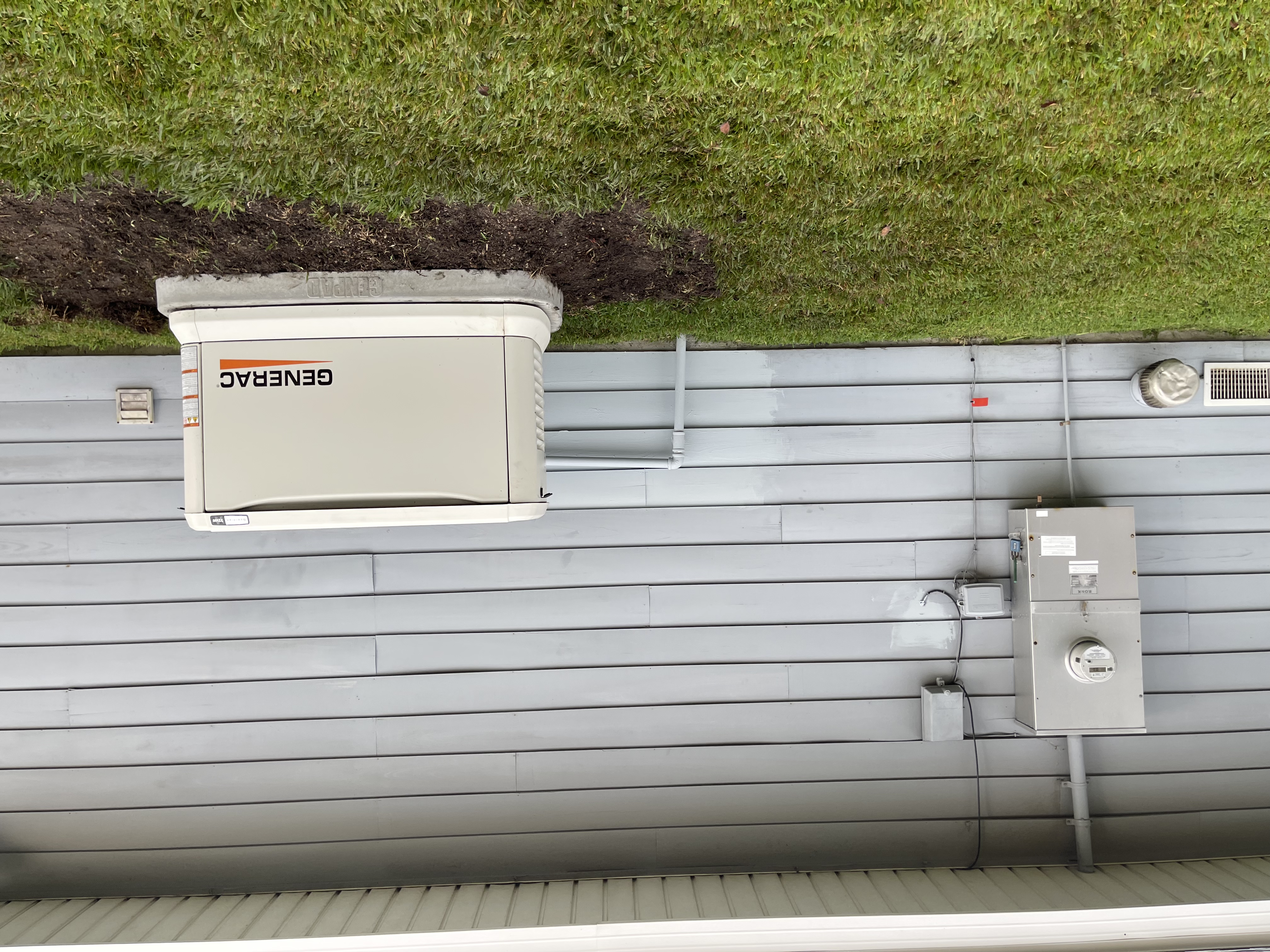 Generac standby generator on a concrete pad next to a house with light gray siding.
